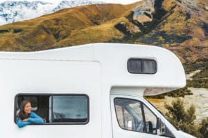 RV road trip tourist woman looking out the window of her motorhome on New Zealand travel. Happy young Asian girl traveling outdoors in adventure vacation driving a campervan. Home away from home.
